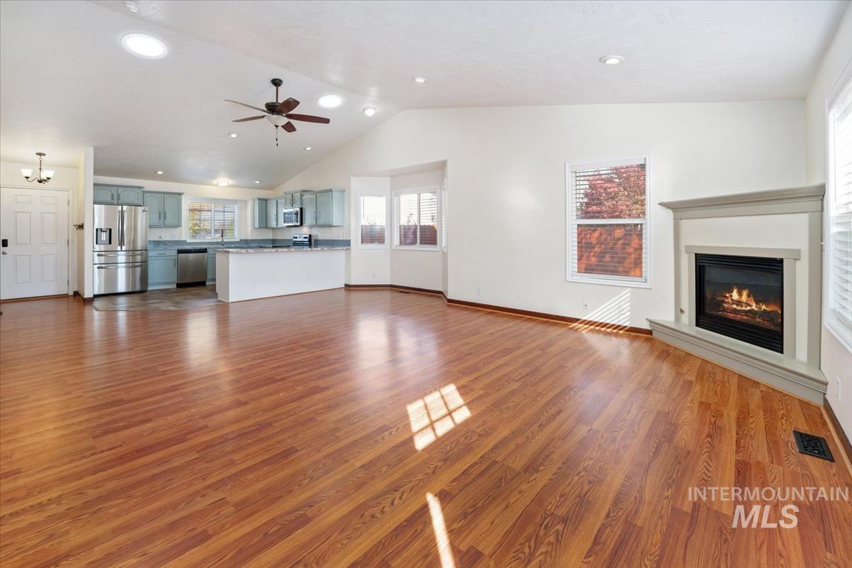 Unfurnished living room with light wood finished floors, a glass covered fireplace, recessed lighting, ceiling fan, and high vaulted ceiling