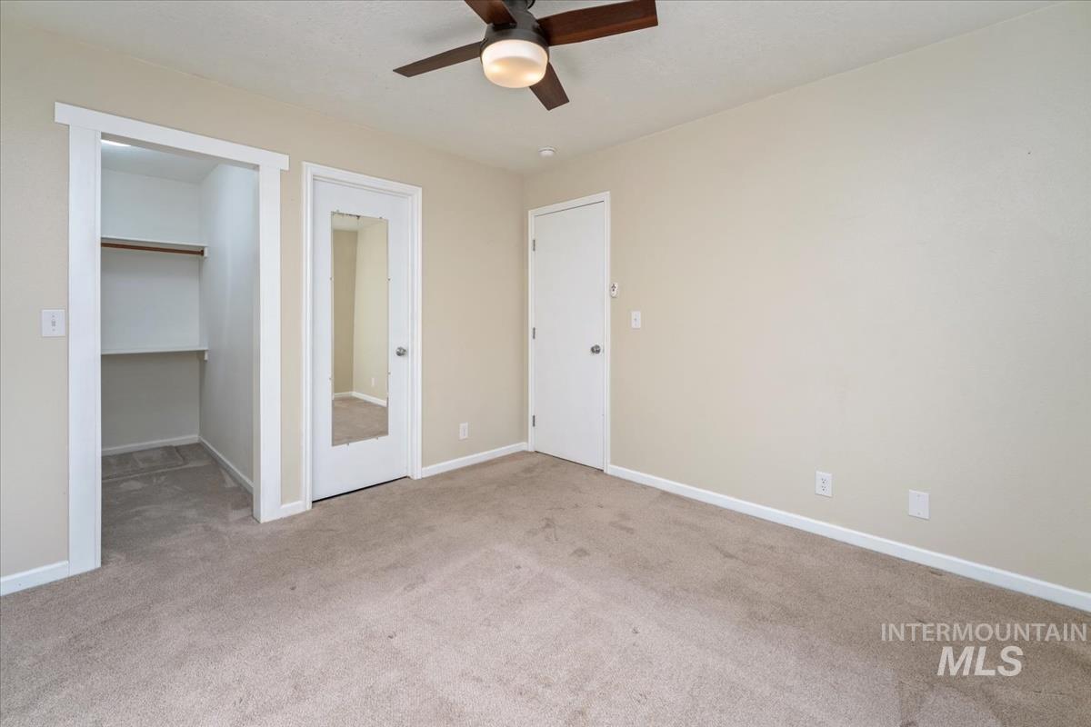 Unfurnished bedroom with a walk in closet, light colored carpet, and a ceiling fan