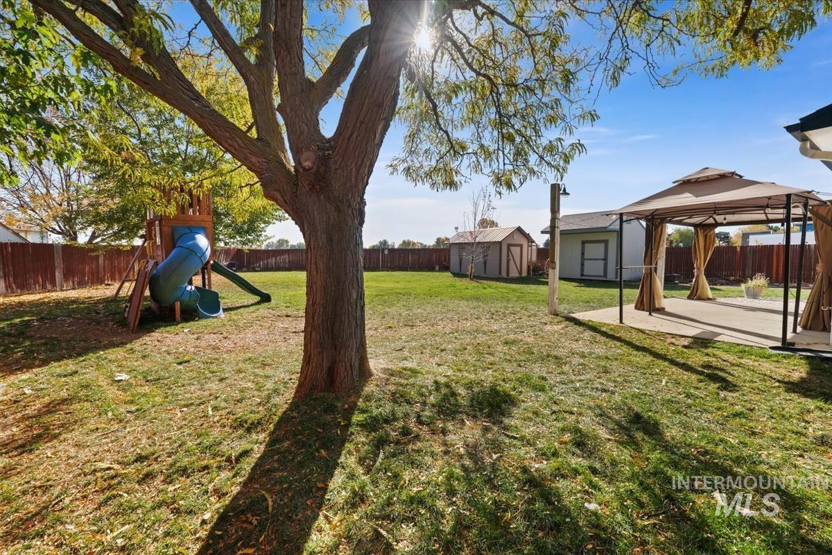 Fenced backyard with a shed, a gazebo, a patio, and a playground