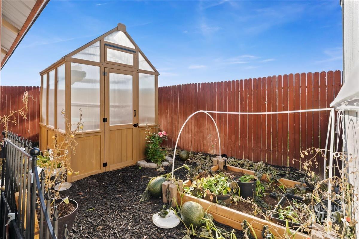 Fenced backyard with a vegetable garden, a greenhouse, and an outdoor structure