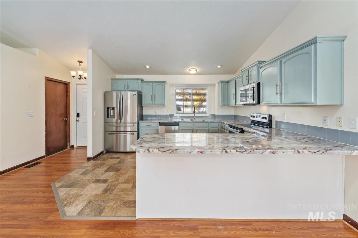 Kitchen featuring appliances with stainless steel finishes, light wood-type flooring, light stone countertops, vaulted ceiling, and a peninsula