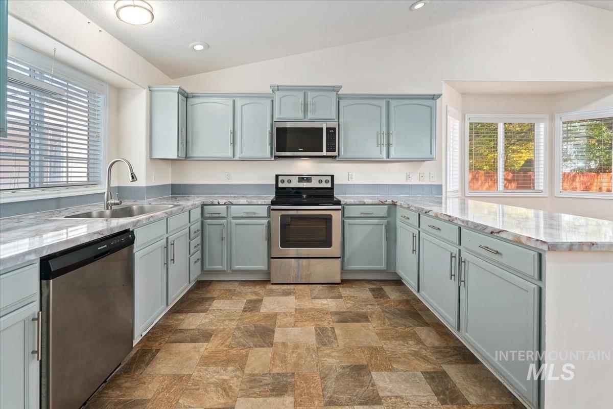 Kitchen featuring stainless steel appliances, plenty of natural light, lofted ceiling, stone finish floors, and recessed lighting
