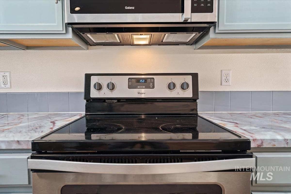 Kitchen view of appliances with stainless steel finishes, a textured wall, and light stone countertops