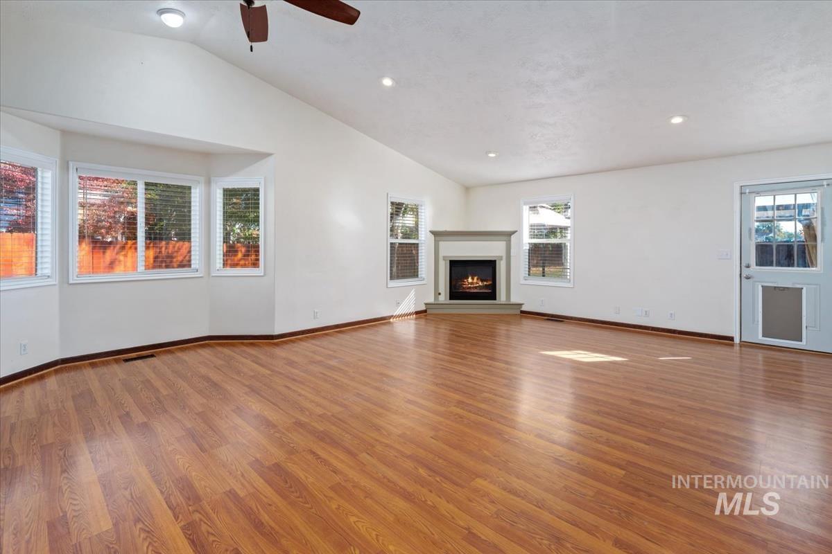 Unfurnished living room with light wood-style floors, a warm lit fireplace, lofted ceiling, recessed lighting, and a ceiling fan