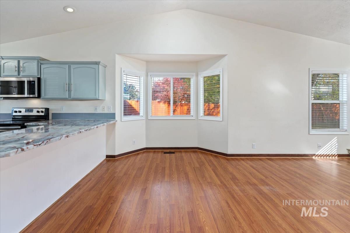 Kitchen featuring lofted ceiling, dark wood-style flooring, stainless steel appliances, and light stone counters