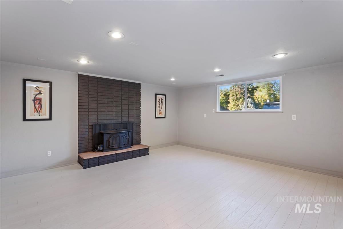 Unfurnished living room with a wood stove, ornamental molding, light wood-style flooring, and recessed lighting