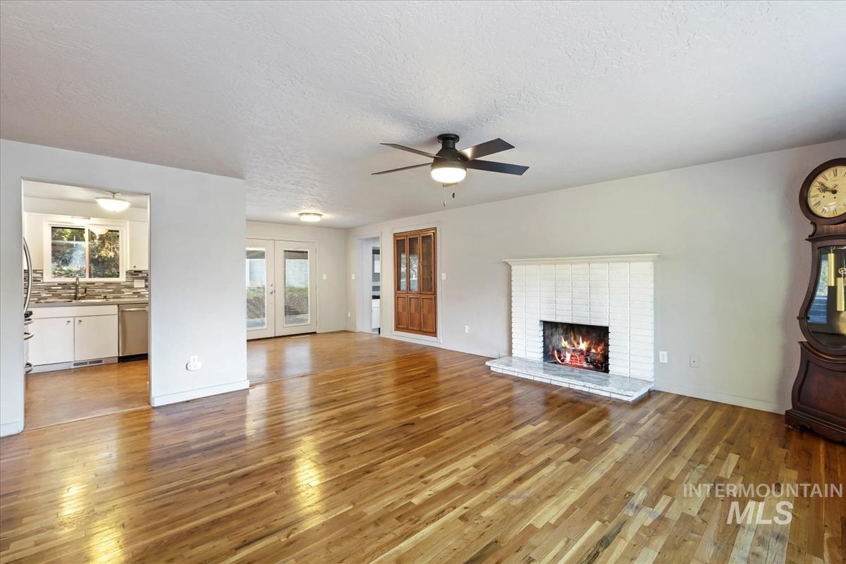 Unfurnished living room featuring light wood finished floors, healthy amount of natural light, french doors, a textured ceiling, and a brick fireplace
