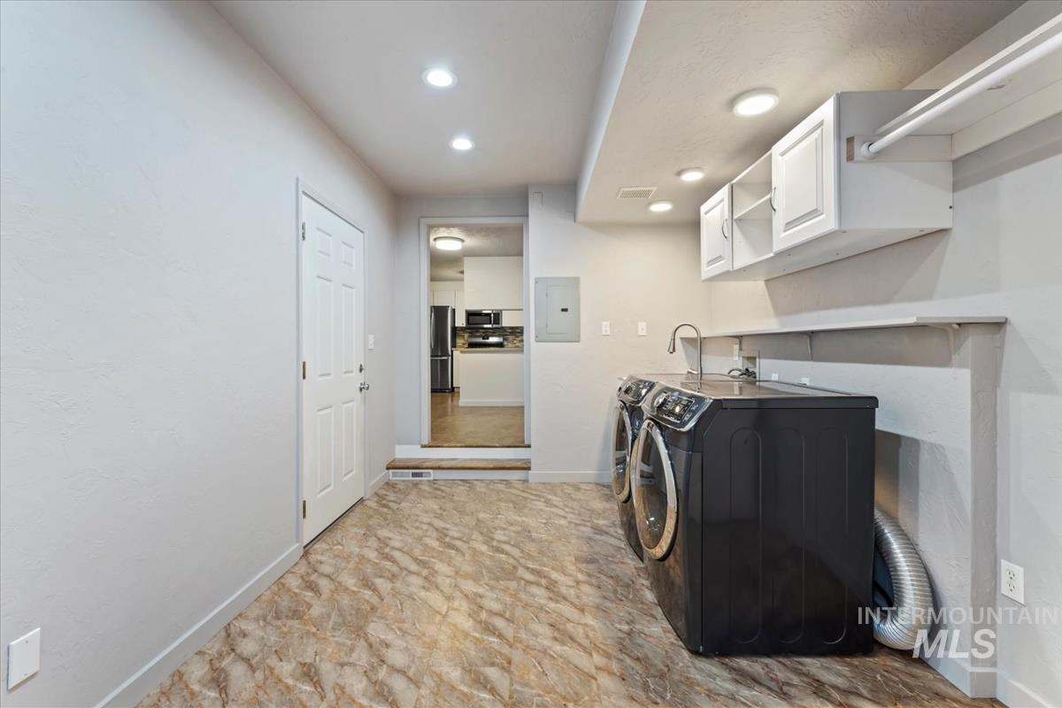 Washroom with cabinet space, electric panel, washer and dryer, and recessed lighting