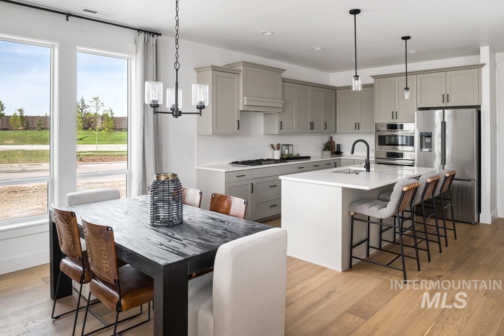 Kitchen featuring appliances with stainless steel finishes, gray cabinets, a kitchen breakfast bar, light wood-style floors, and light countertops
