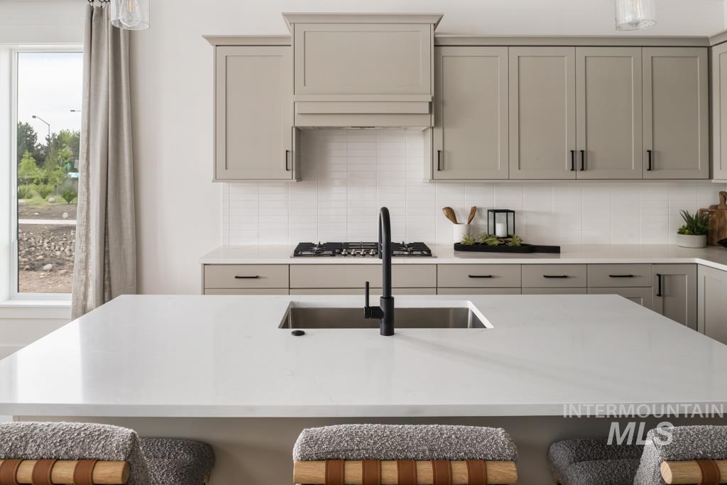 Kitchen featuring custom cabinetry, stainless steel gas stovetop, quartz countertops, and tasteful backsplash
