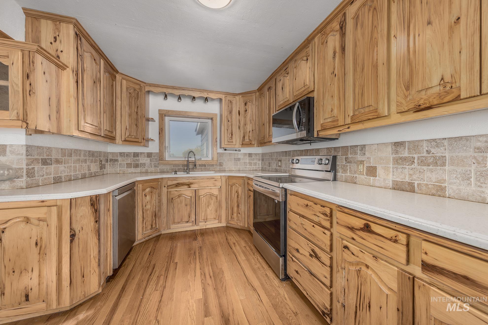 Kitchen with appliances with stainless steel finishes, light wood-type flooring, light stone counters, and decorative backsplash