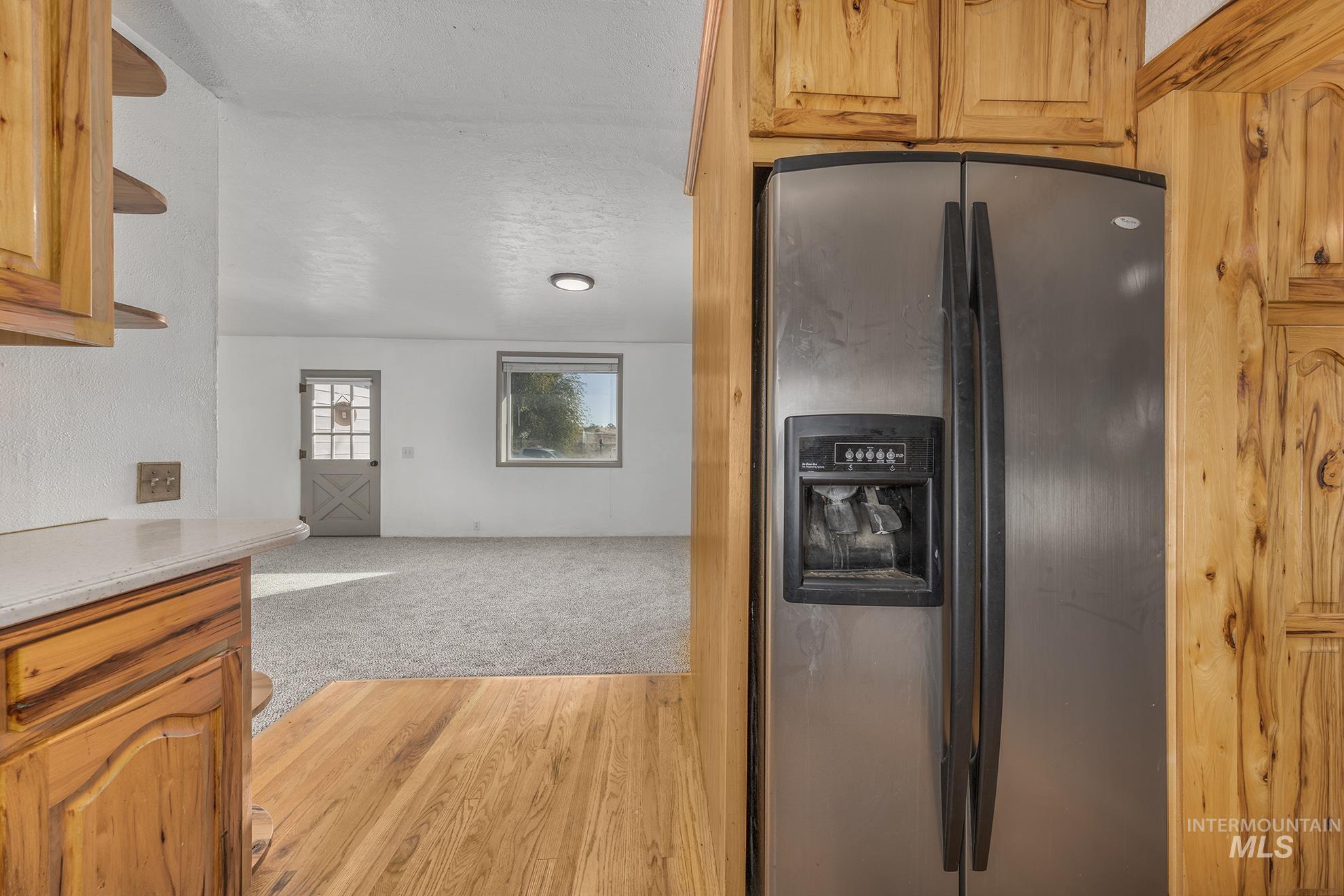 Kitchen with stainless steel refrigerator with ice dispenser, a textured ceiling, light countertops, light wood-style flooring, and light colored carpet