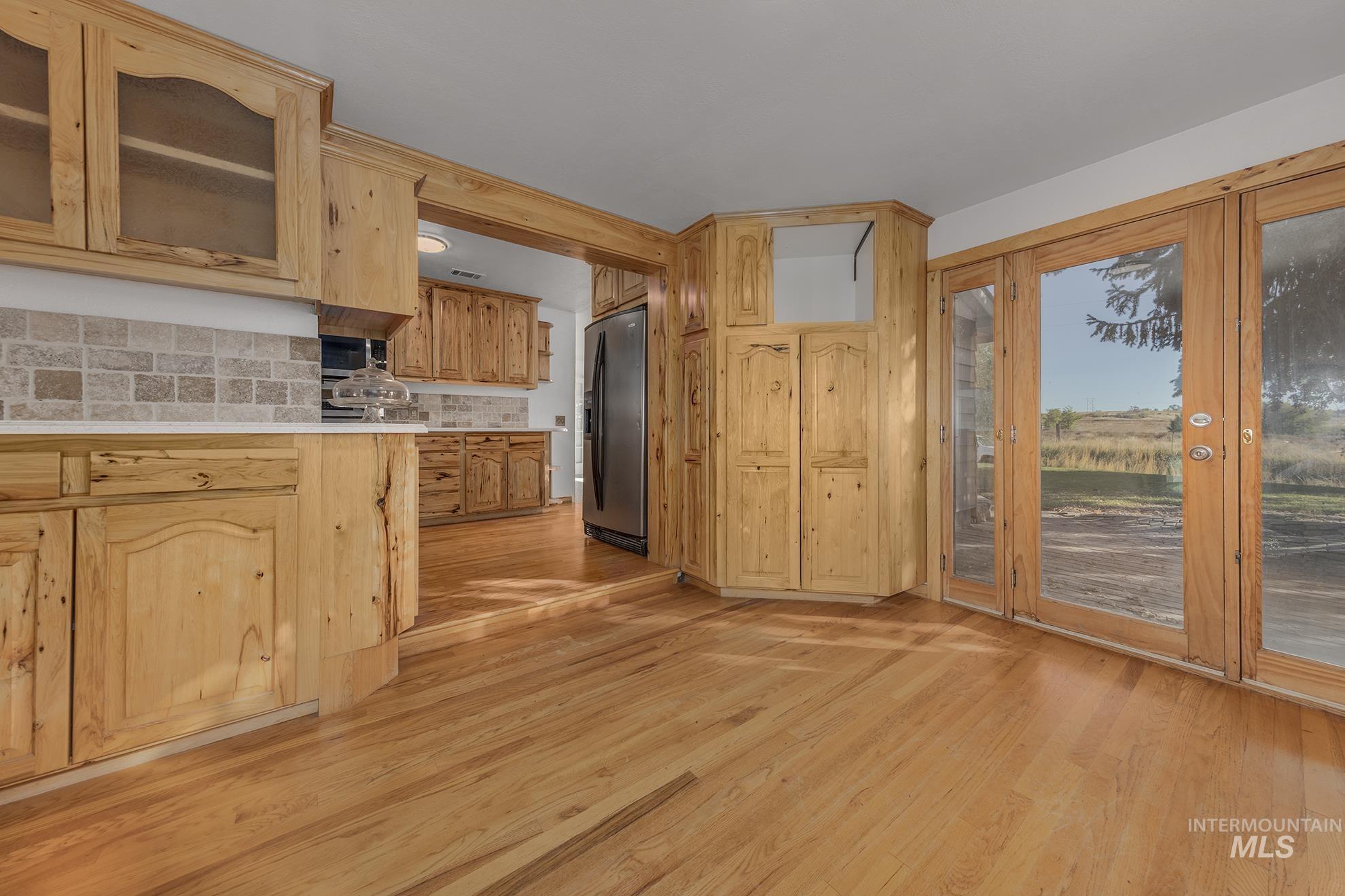 Kitchen with glass insert cabinets, light wood finished floors, backsplash, stainless steel refrigerator with ice dispenser, and light brown cabinets