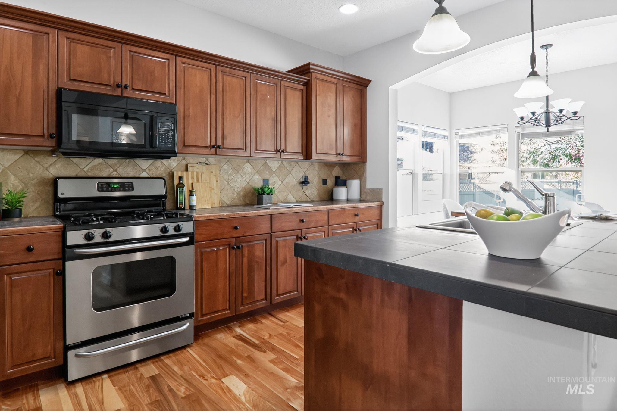 Kitchen featuring stainless steel gas range oven, brown cabinetry, black microwave, pendant lighting, and light wood-style floors