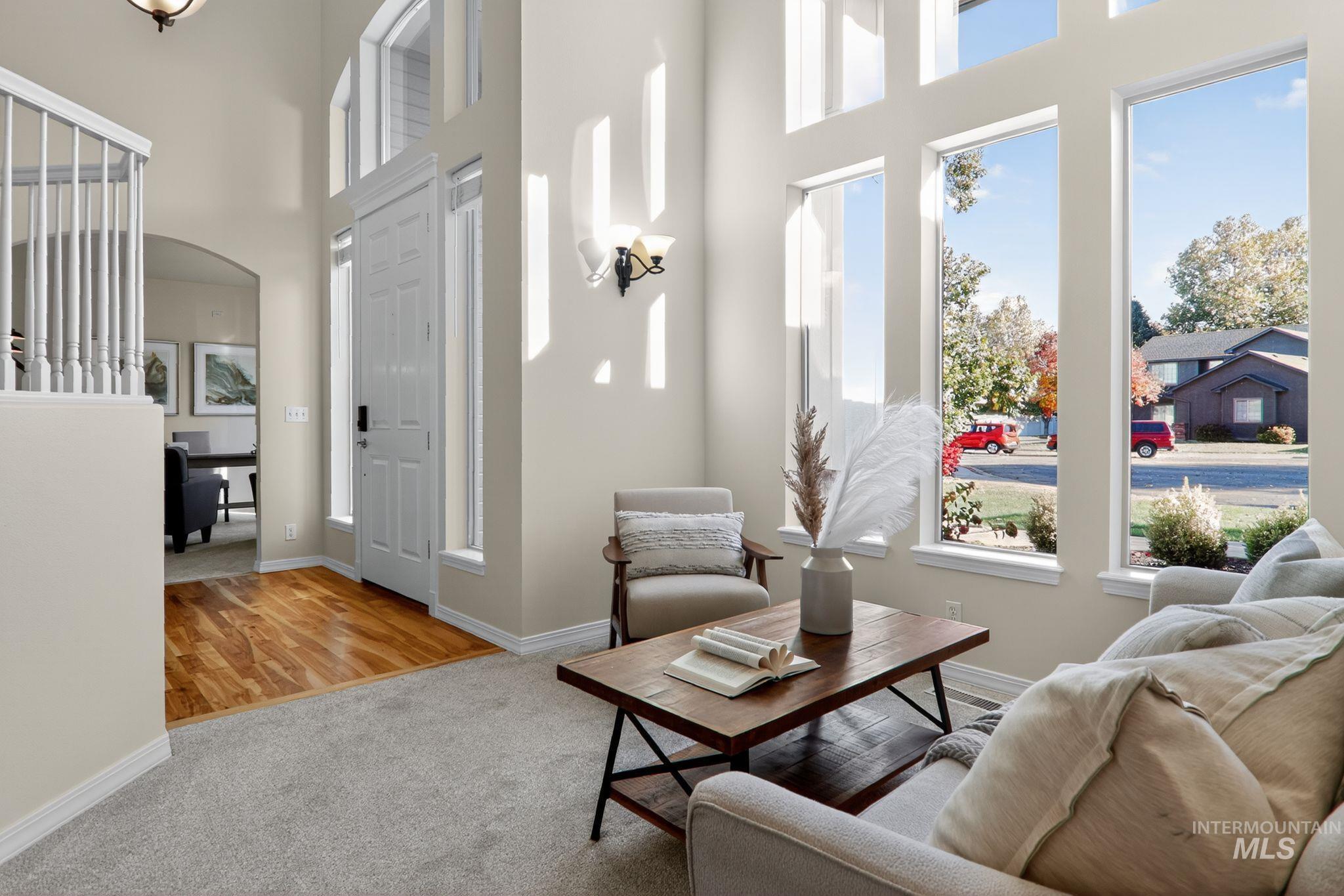 Living room with light carpet, arched walkways, light wood-style flooring, and a towering ceiling