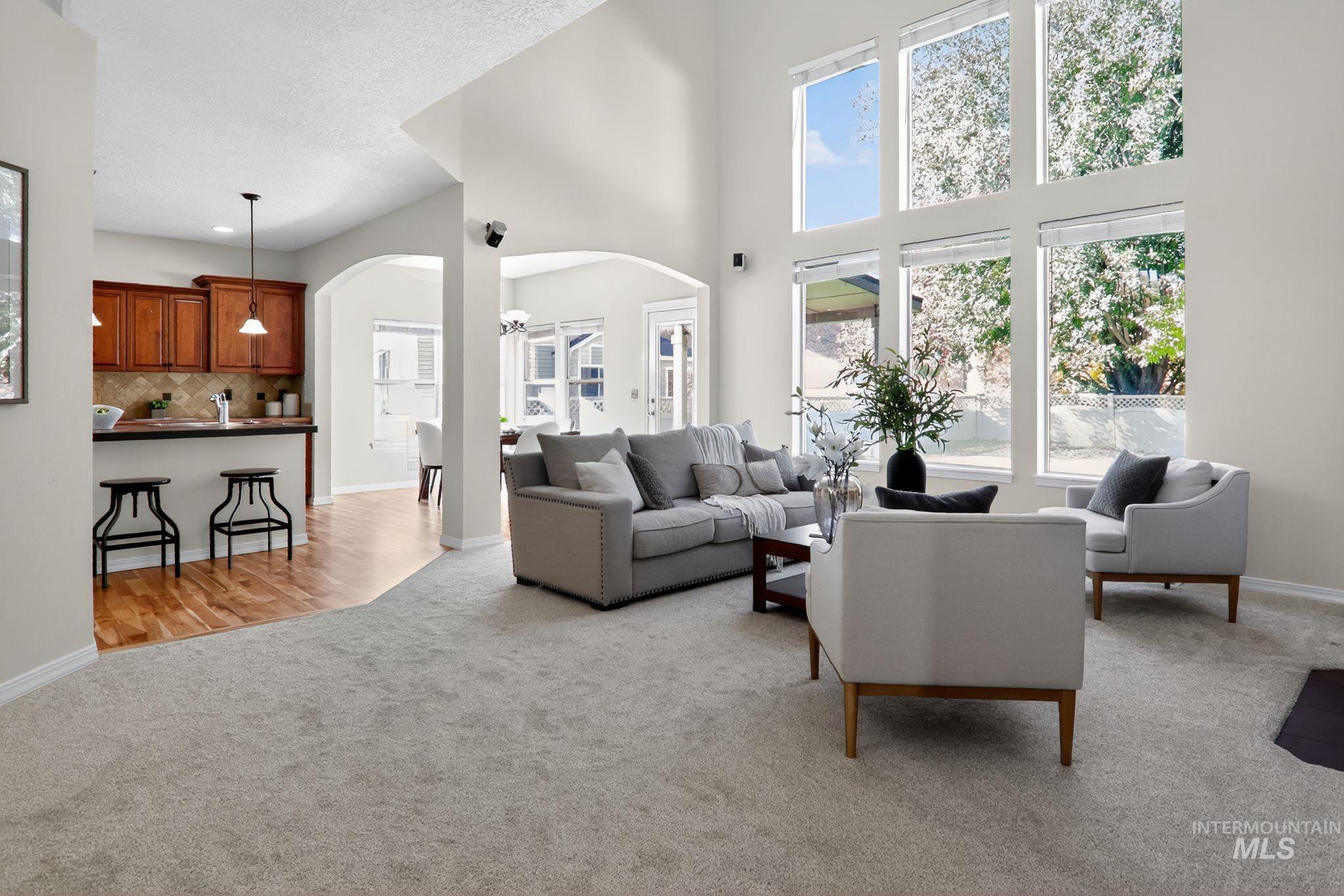 Living room featuring light colored carpet, arched walkways, healthy amount of natural light, light wood finished floors, and a towering ceiling