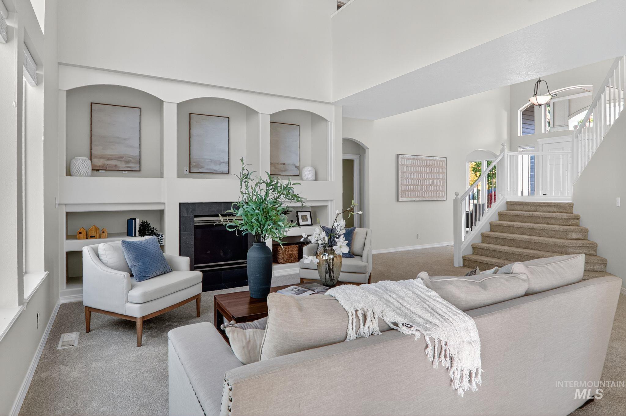 Carpeted living room with built in shelves, a high ceiling, stairway, a fireplace, and arched walkways