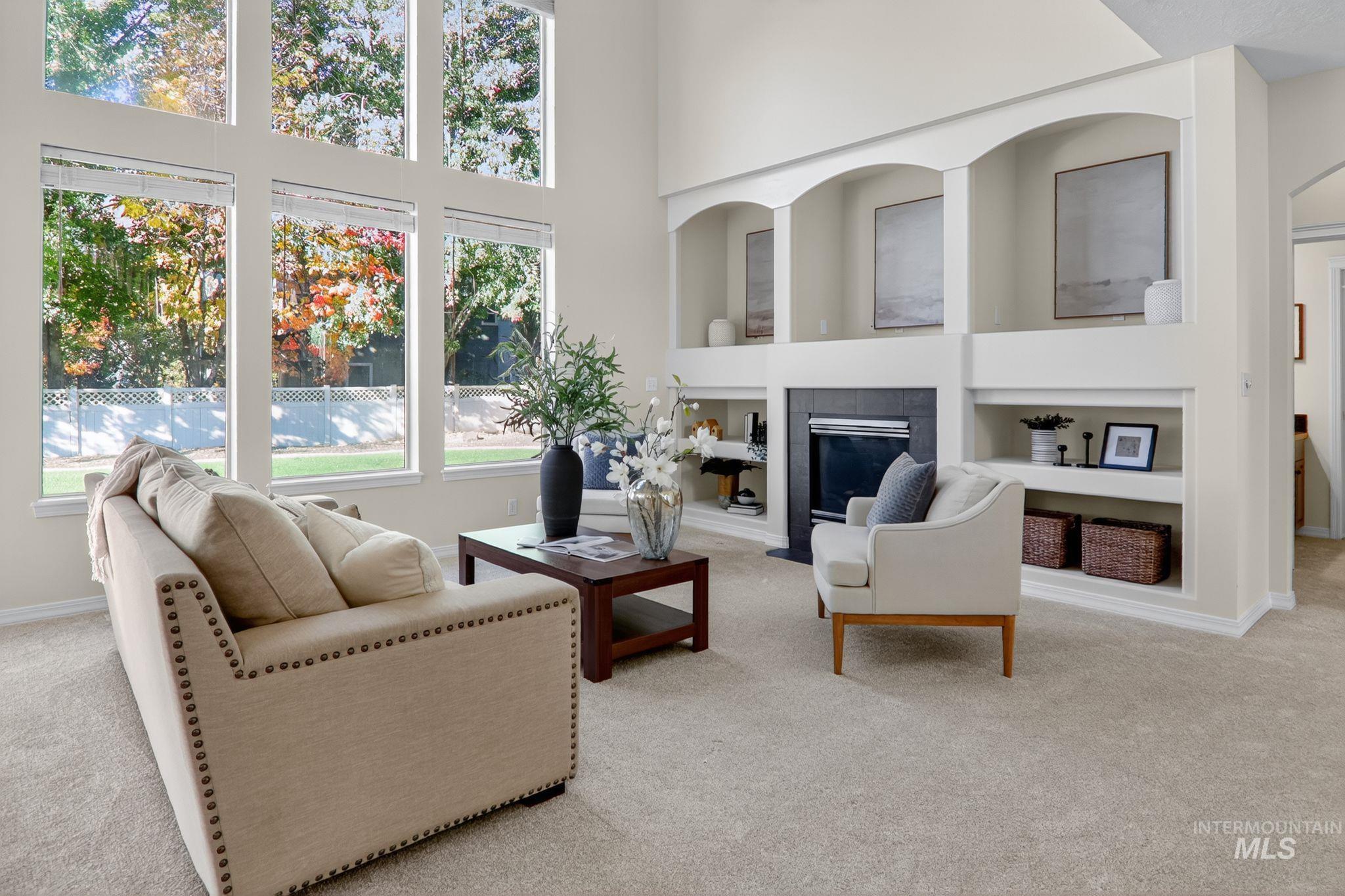 Living room featuring built in shelves, a tile fireplace, light carpet, and a high ceiling
