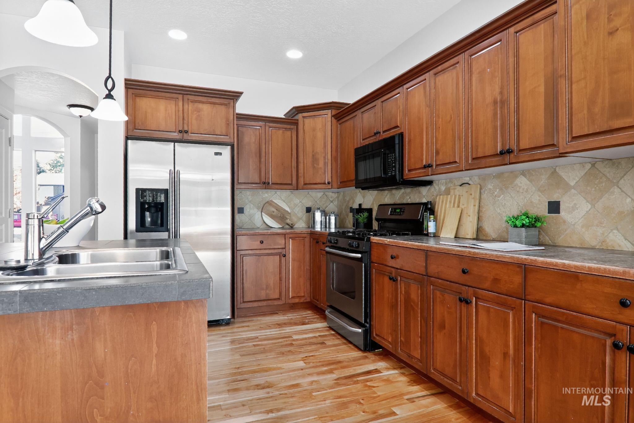 Kitchen with appliances with stainless steel finishes, brown cabinetry, pendant lighting, light wood finished floors, and backsplash