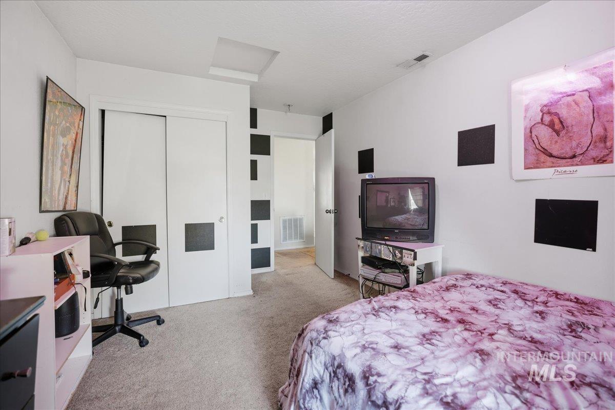 Bedroom featuring light carpet, a closet, a desk, attic access, and a textured ceiling