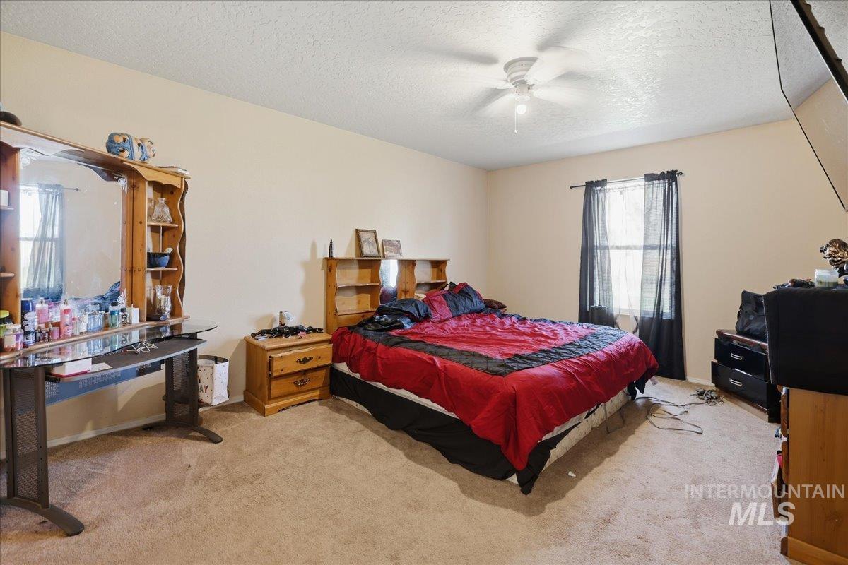 Bedroom with a textured ceiling, light colored carpet, and a ceiling fan