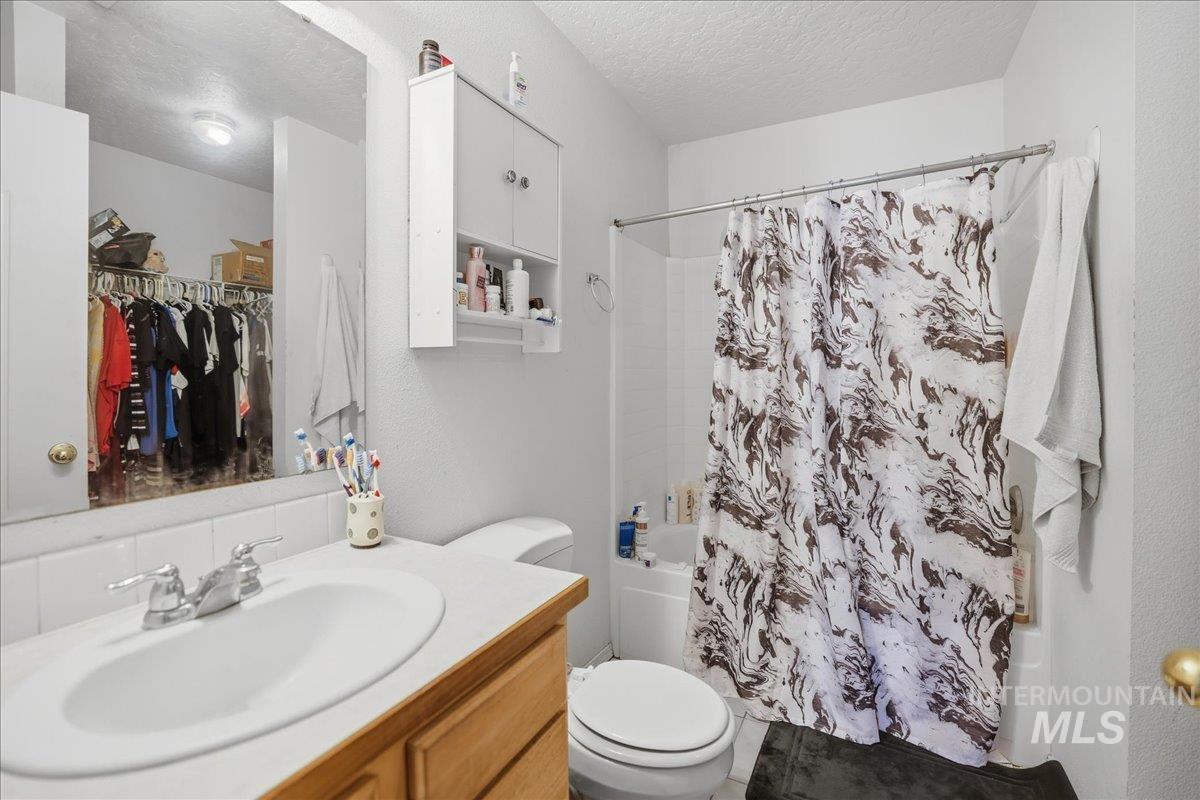 Bathroom featuring shower / bath combo, vanity, a textured ceiling, and a walk in closet