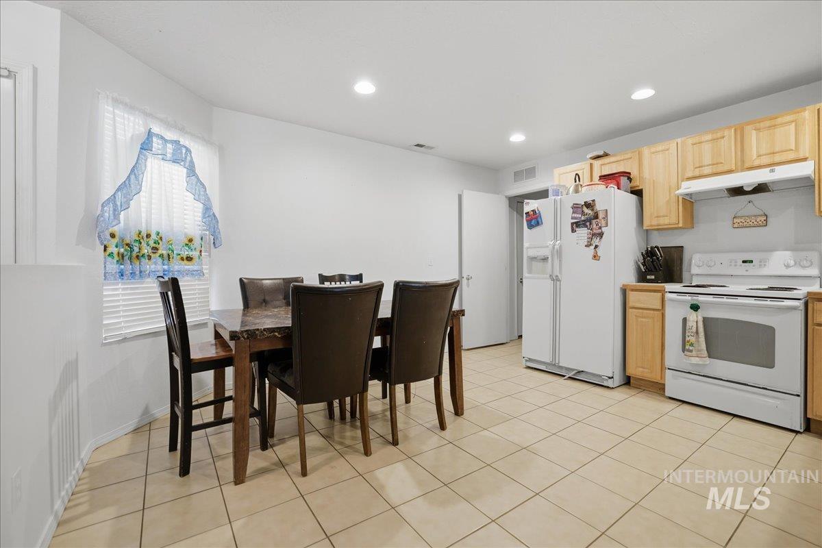 Kitchen featuring white appliances, light brown cabinets, under cabinet range hood, light tile patterned floors, and light countertops
