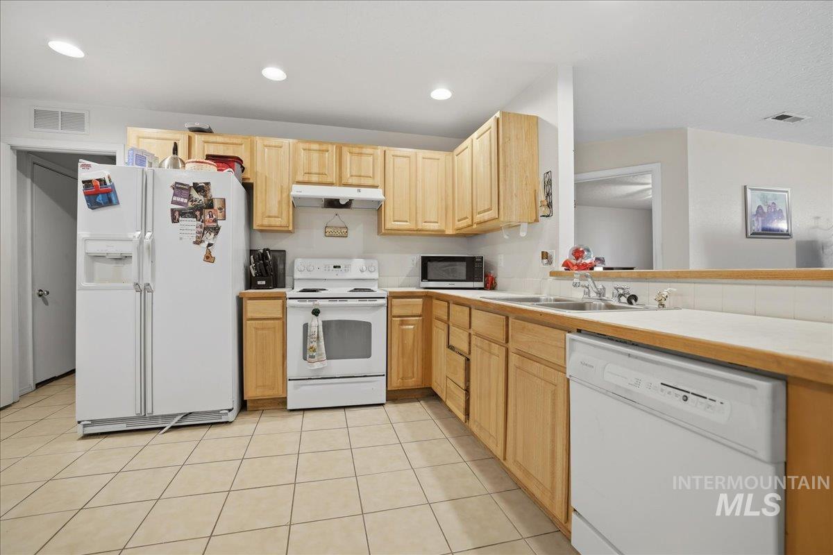 Kitchen featuring white appliances, light brown cabinets, light tile patterned floors, under cabinet range hood, and recessed lighting