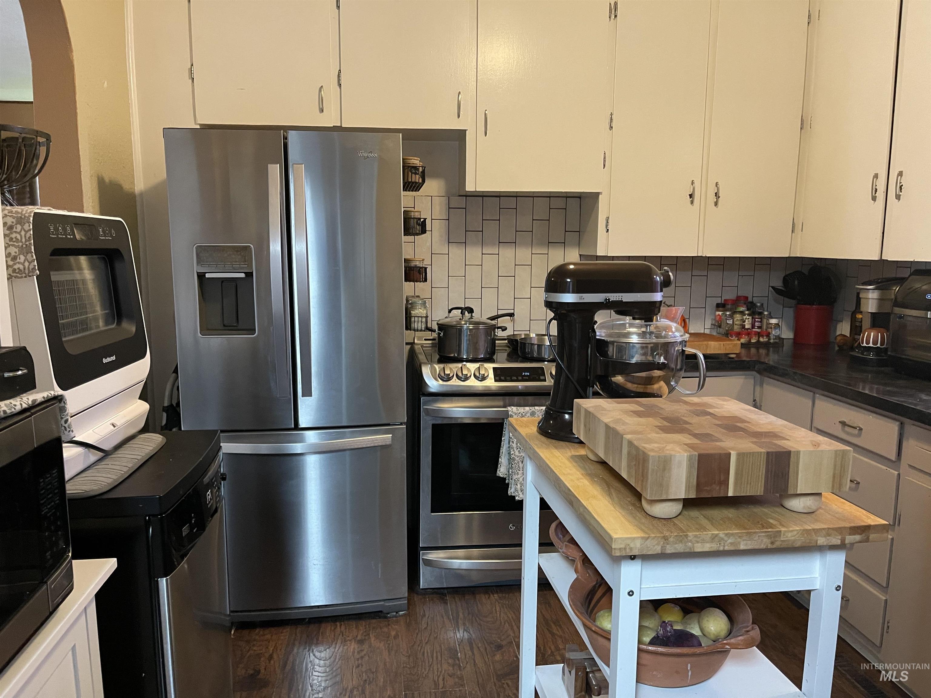 Kitchen with stainless steel appliances, white cabinets, tasteful backsplash, and dark wood finished floors