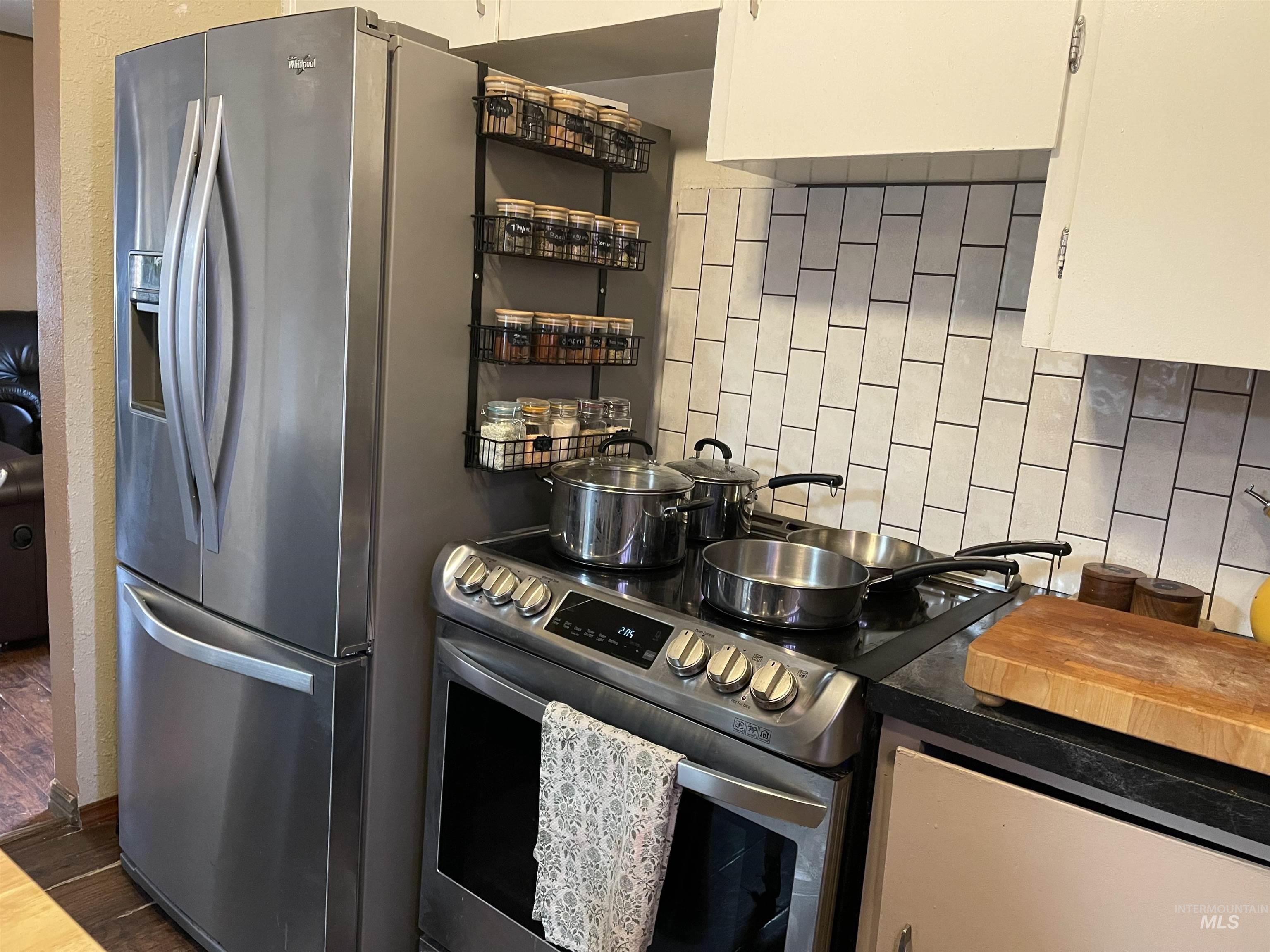 Kitchen with appliances with stainless steel finishes, backsplash, dark countertops, and dark wood-style floors