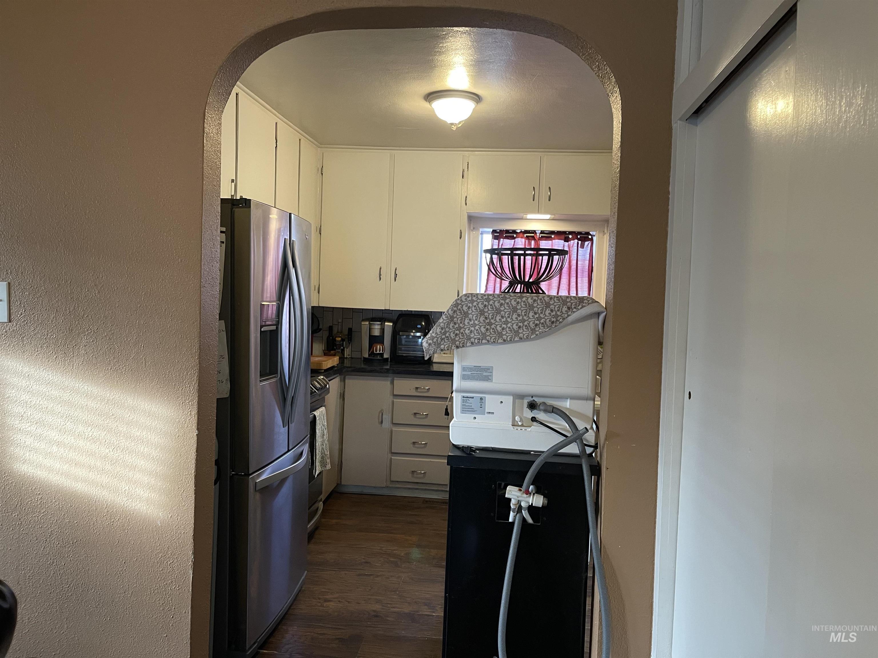 Kitchen featuring dark countertops, arched walkways, appliances with stainless steel finishes, dark wood-style floors, and a textured wall