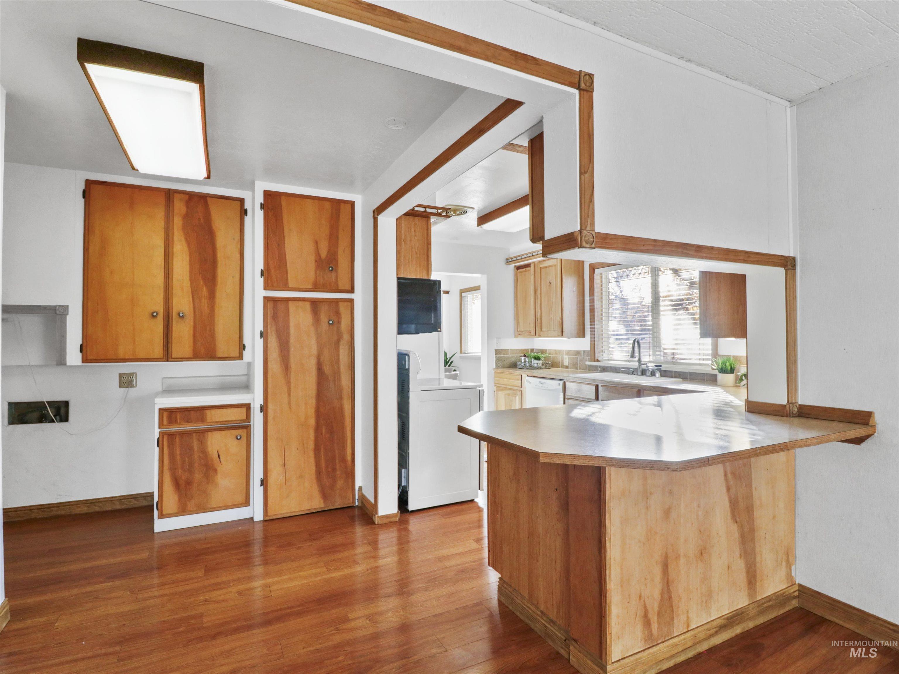 Kitchen featuring a peninsula, light countertops, dark wood-type flooring, and brown cabinetry