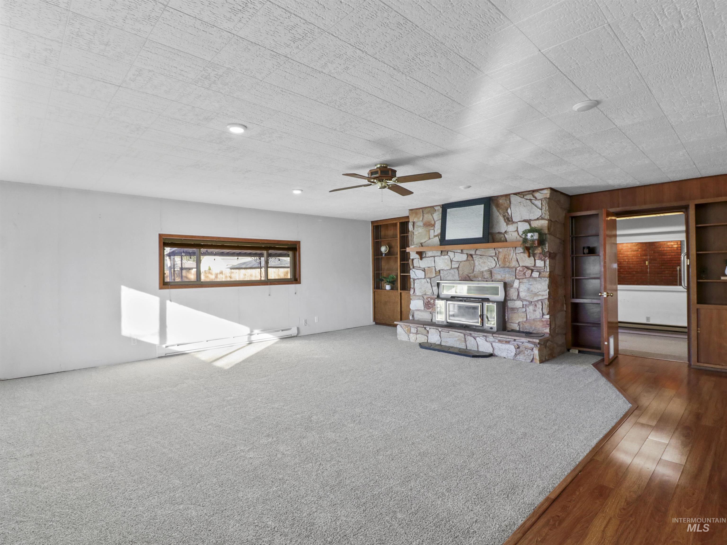 Unfurnished living room with built in shelves, a stone fireplace, ceiling fan, and carpet floors