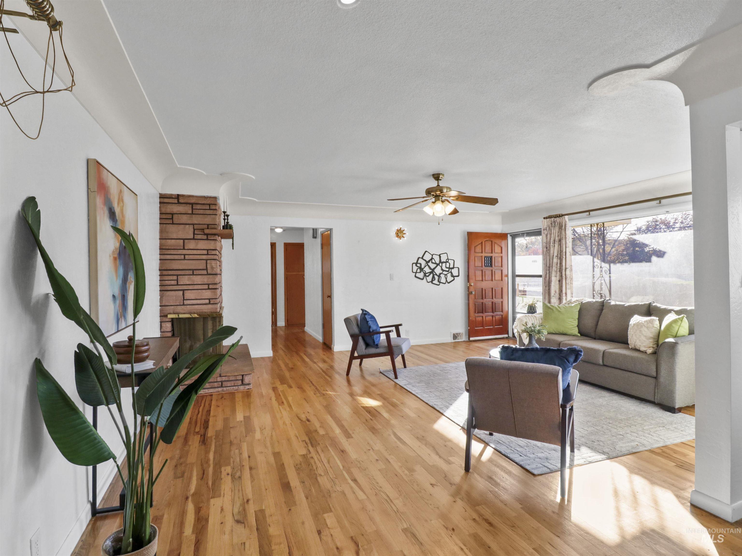 Living room featuring light wood-style floors, a stone fireplace, and ceiling fan