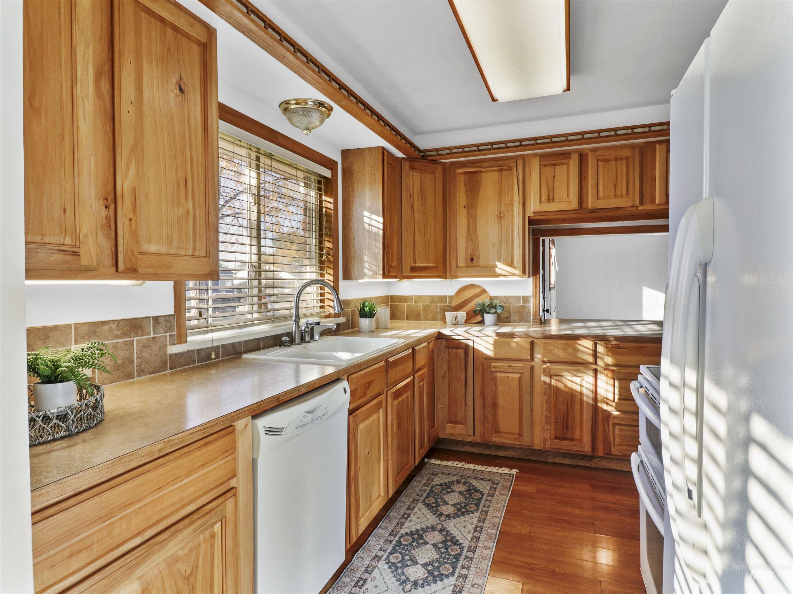 Kitchen featuring white appliances, light countertops, dark wood-style floors, backsplash, and brown cabinets