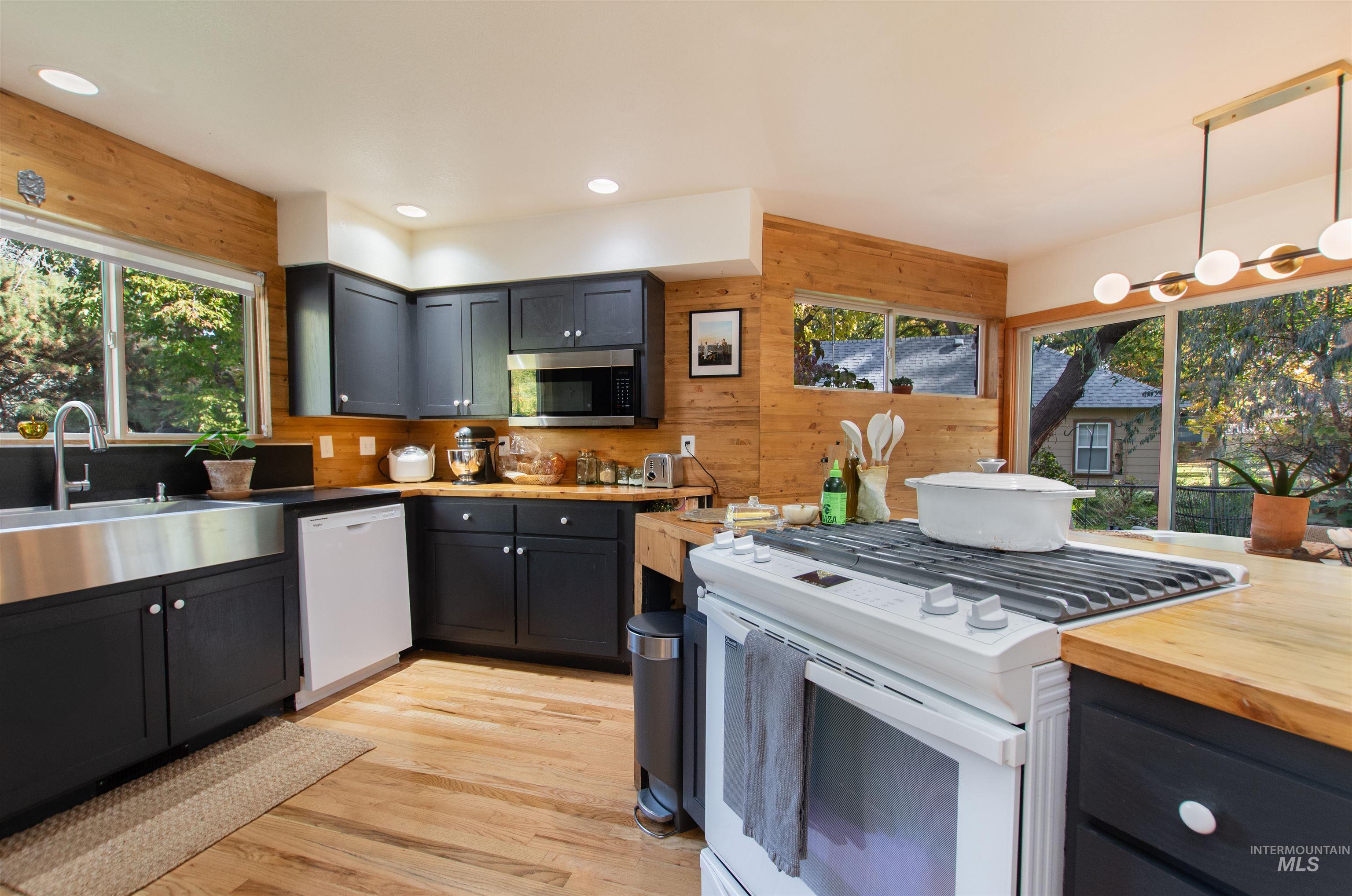 Kitchen featuring white appliances, wood walls, light wood finished floors, healthy amount of natural light, and decorative light fixtures