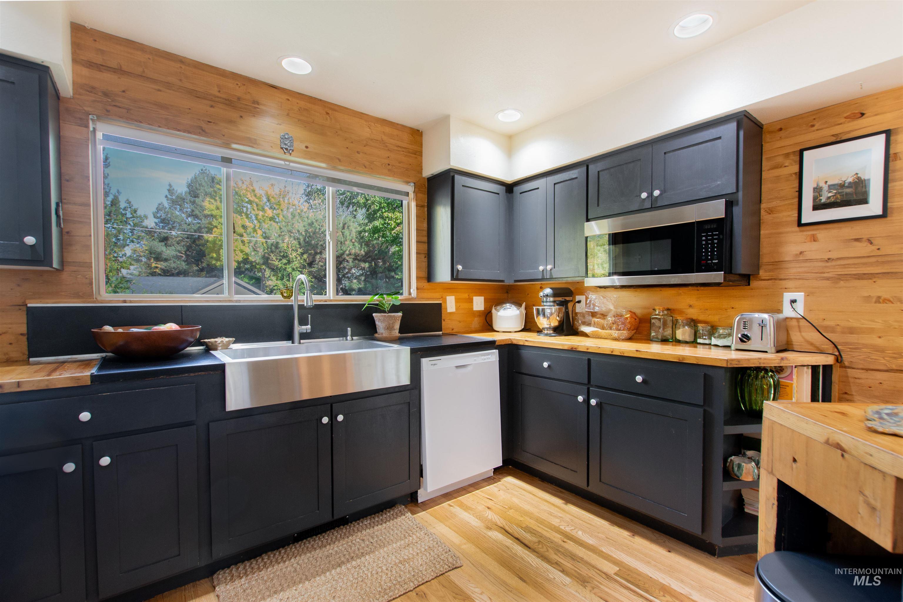 Kitchen with wooden walls, light wood-type flooring, dishwasher, butcher block countertops, and stainless steel microwave