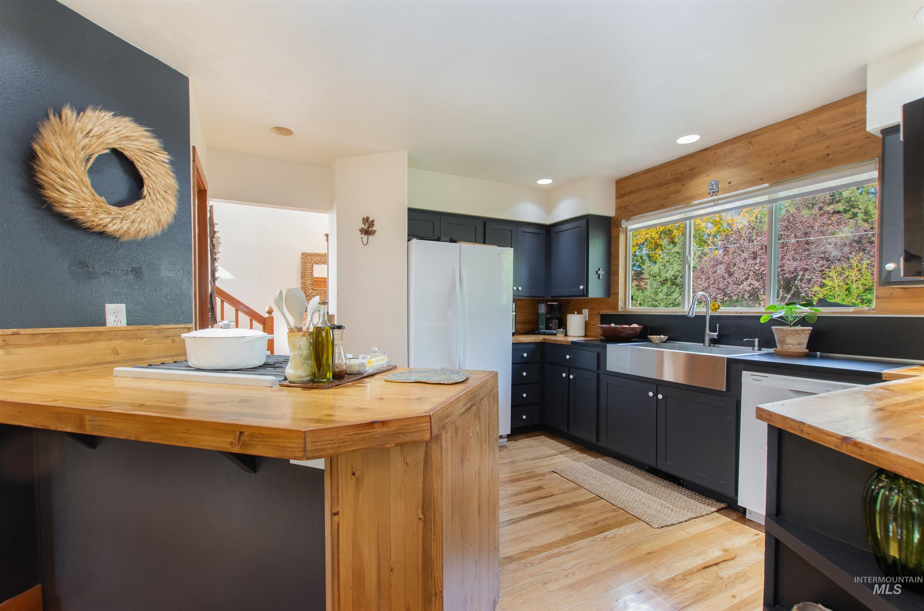 Kitchen with butcher block countertops, light wood finished floors, white appliances, a breakfast bar, and recessed lighting