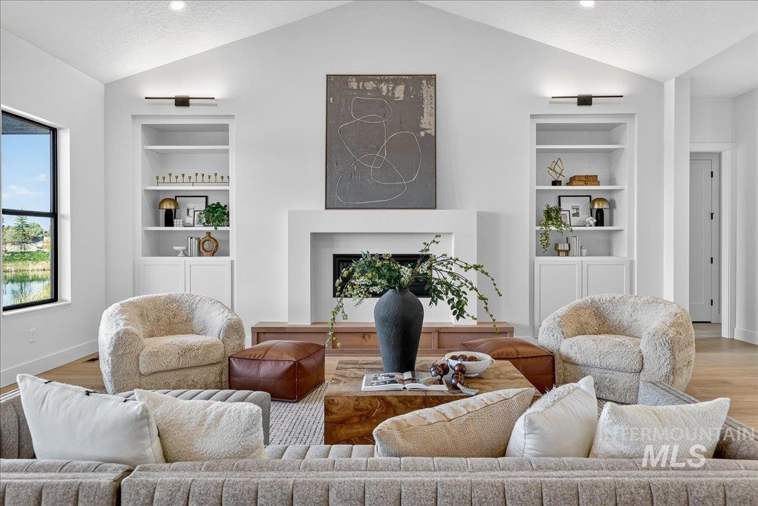 Living room with built in features, light wood-style floors, vaulted ceiling, a textured ceiling, and a fireplace