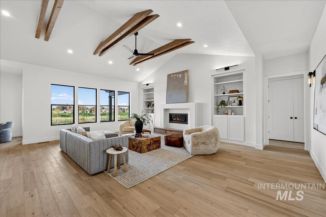 Living room with ceiling fan, built in features, a glass covered fireplace, light wood-style floors, and recessed lighting