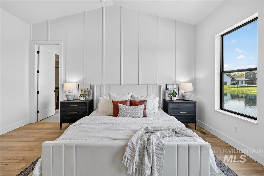 Bedroom featuring light wood finished floors, vaulted ceiling, and a decorative wall