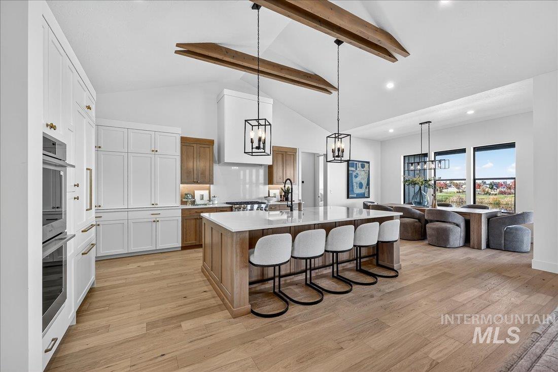 Kitchen featuring beamed ceiling, a breakfast bar area, decorative light fixtures, a kitchen island with sink, and light wood-style floors