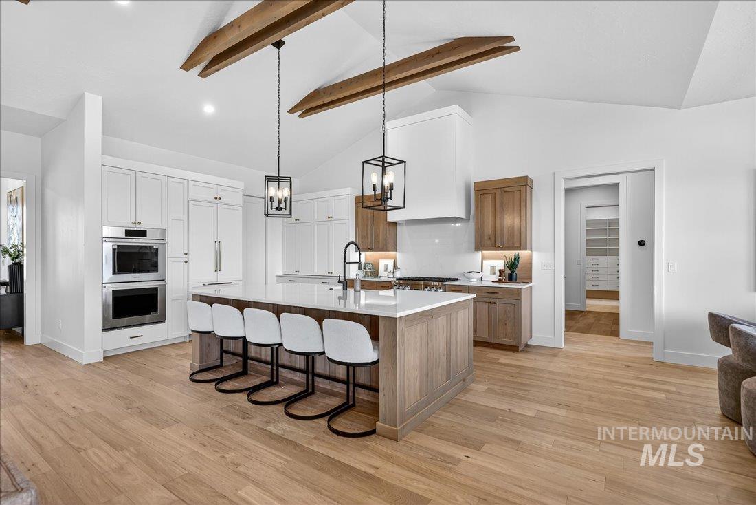 Kitchen with a breakfast bar area, decorative light fixtures, high vaulted ceiling, an island with sink, and stainless steel double oven