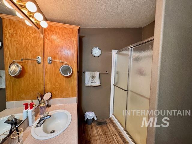 Bathroom with a textured ceiling, a shower stall, vanity, and dark wood-type flooring
