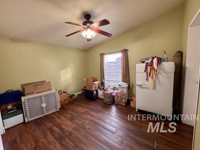 Bedroom featuring lofted ceiling, dark wood-style flooring, a textured ceiling, white refrigerator, and a ceiling fan
