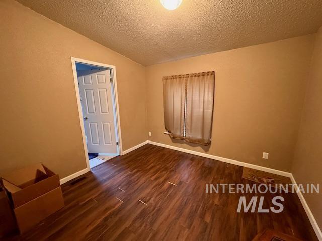 Empty room featuring dark wood-style flooring, a textured ceiling, and lofted ceiling