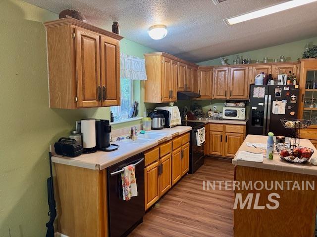 Kitchen with a textured ceiling, black appliances, dark wood-style flooring, brown cabinetry, and vaulted ceiling