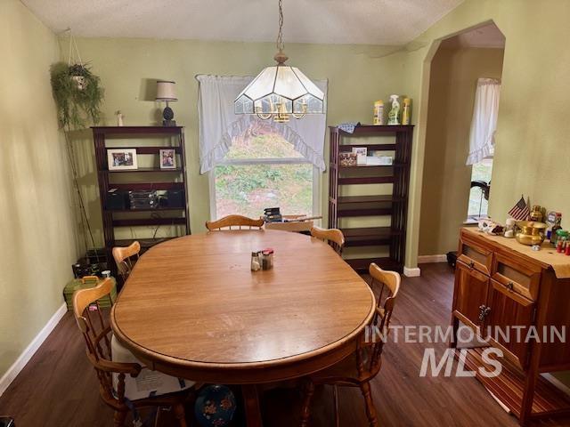 Dining room with dark wood-type flooring, arched walkways, and a chandelier