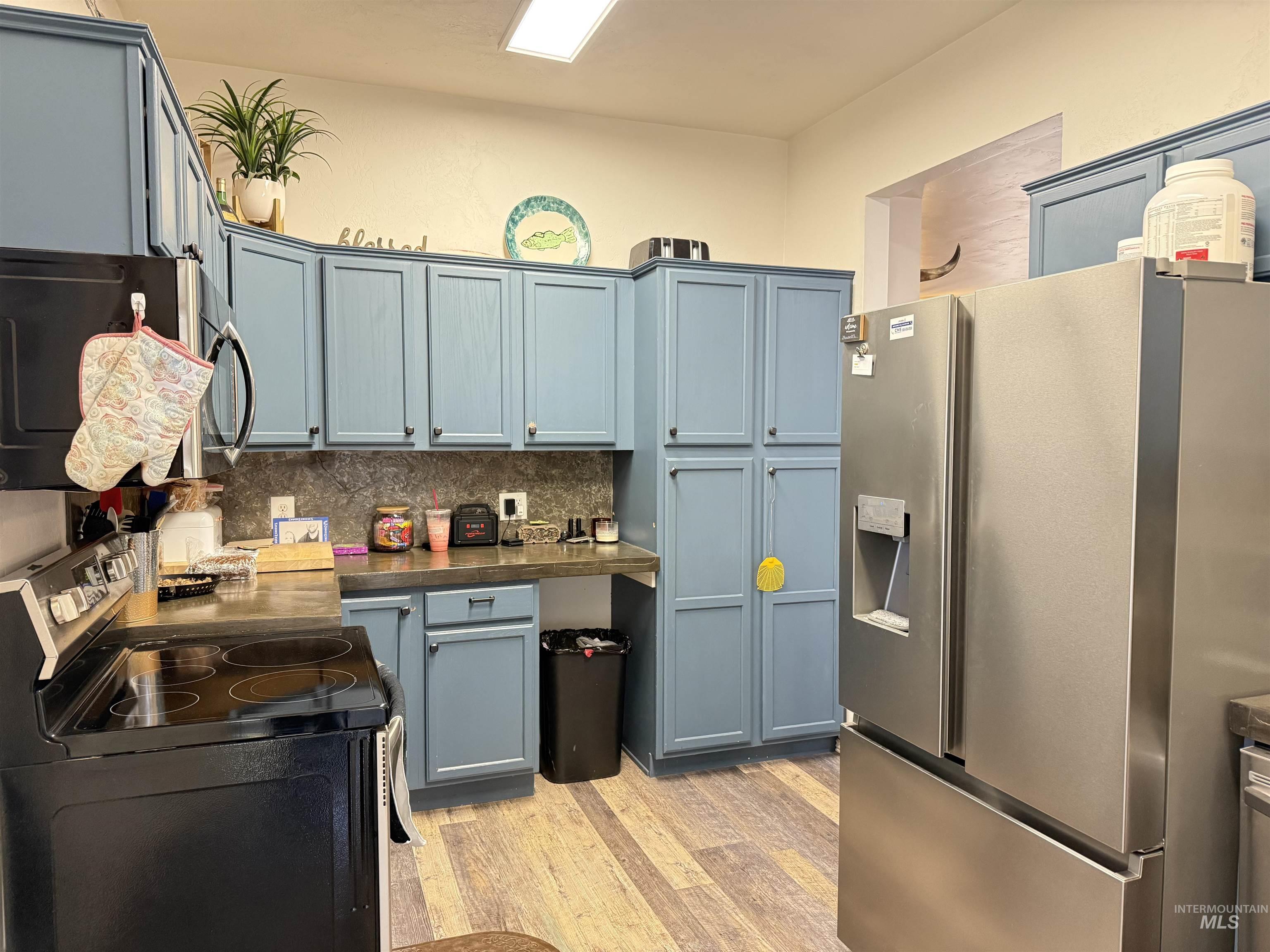 Kitchen with appliances with stainless steel finishes, light wood-style flooring, backsplash, dark countertops, and gray cabinetry