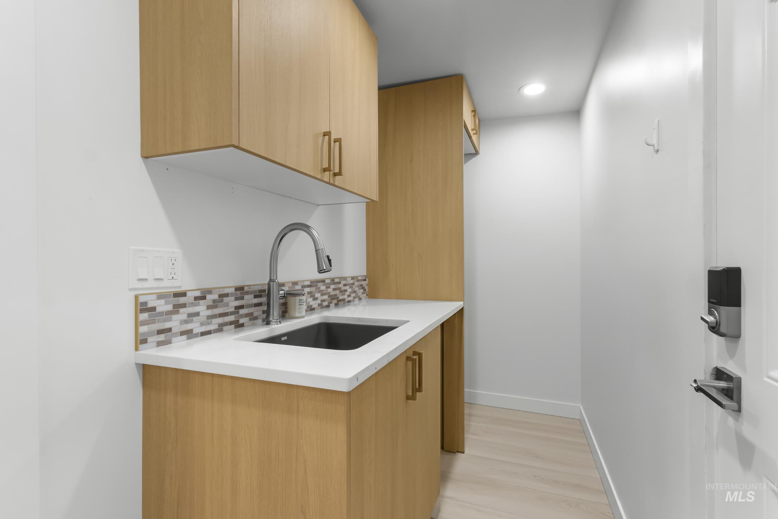 Kitchen with modern cabinets, backsplash, light brown cabinets, light wood-style floors, and light stone countertops